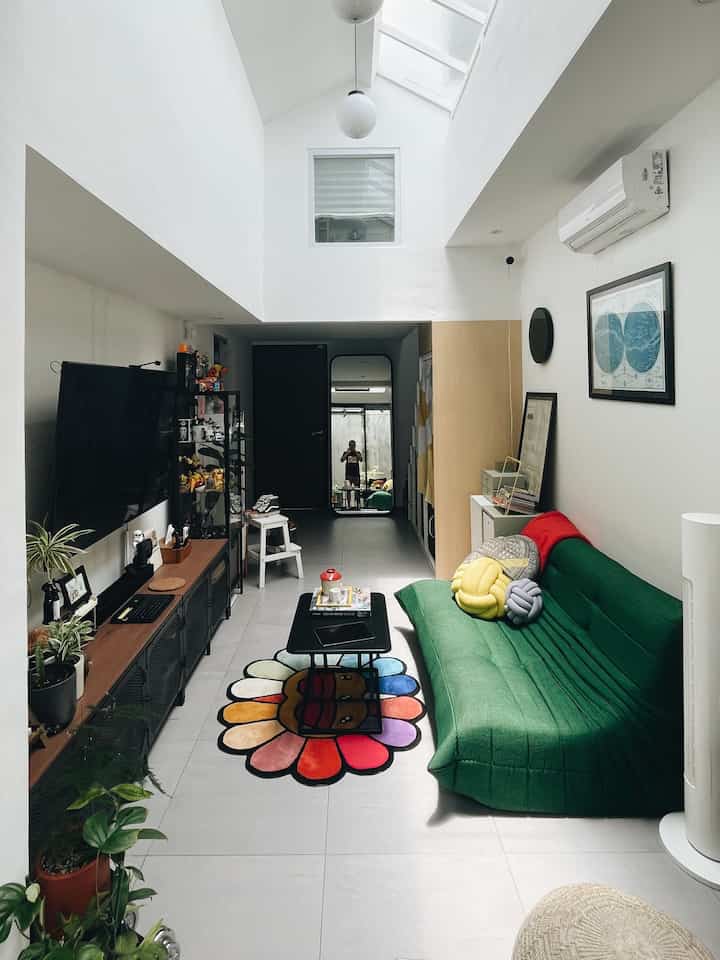 Bright white-toned living room featuring a green sofa and vibrant flower-shaped rug in a modern, compact space