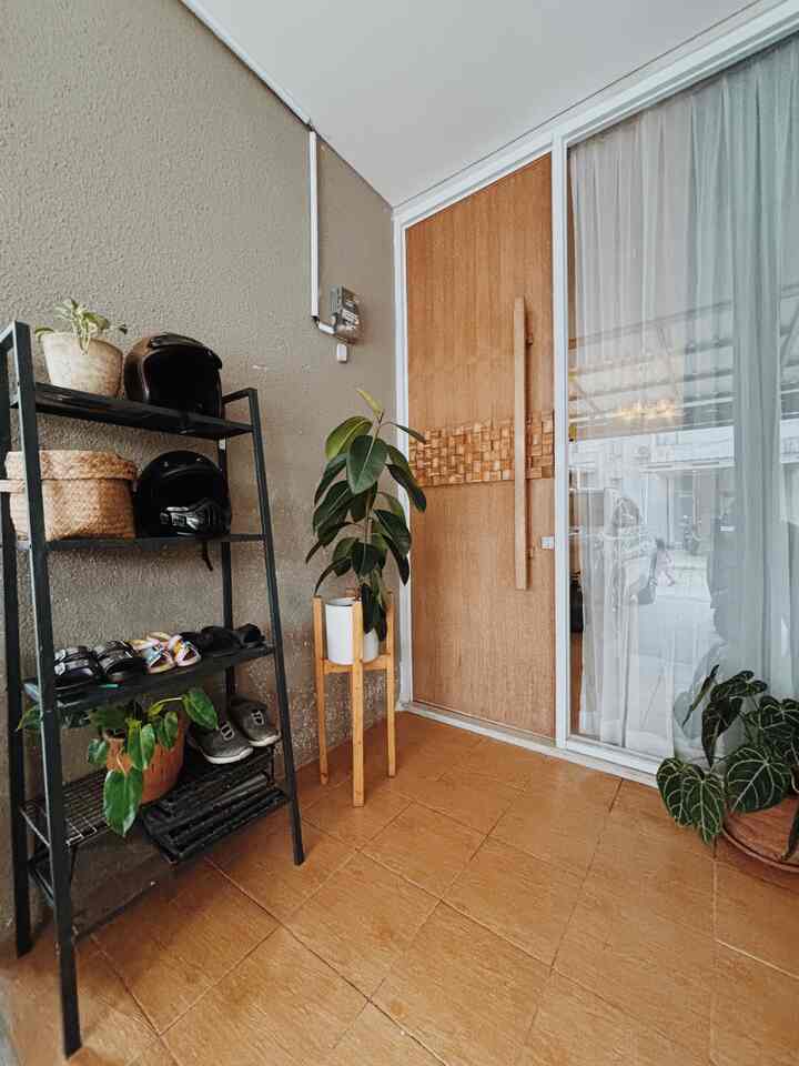 Beige walls and wood-tone floor entrance featuring a black metal shoe rack on the left and potted plants adding cozy touches