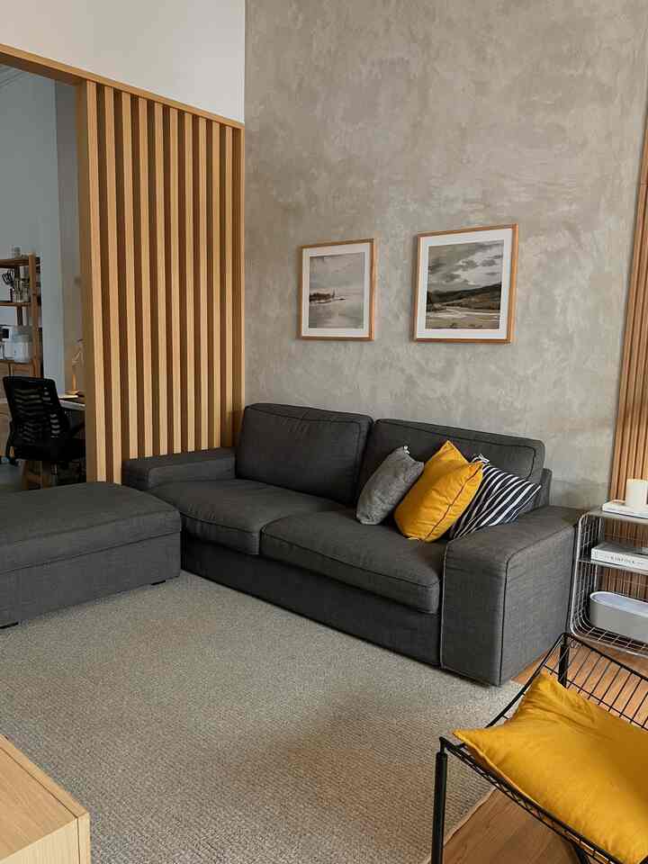 Gray sofa and beige carpet in living room with wooden slats and concrete textured walls, natural modern interior ambiance
