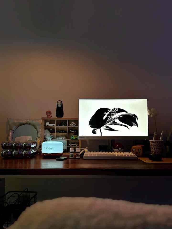 White and dark wood toned home office space featuring white keyboard, monitor, and an electric diffuser on calm work desk