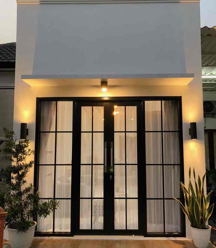 White wall and black-framed entrance featuring wall sconces and plants, creating a tidy exterior space