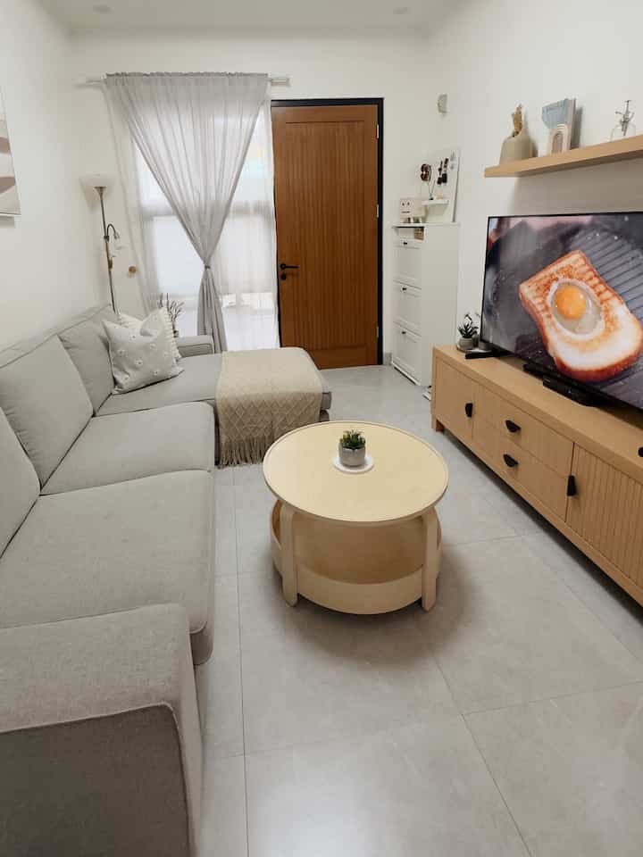 A living room in light gray and wood tones, featuring a simple modern sofa and open plan layout creating a spacious feel