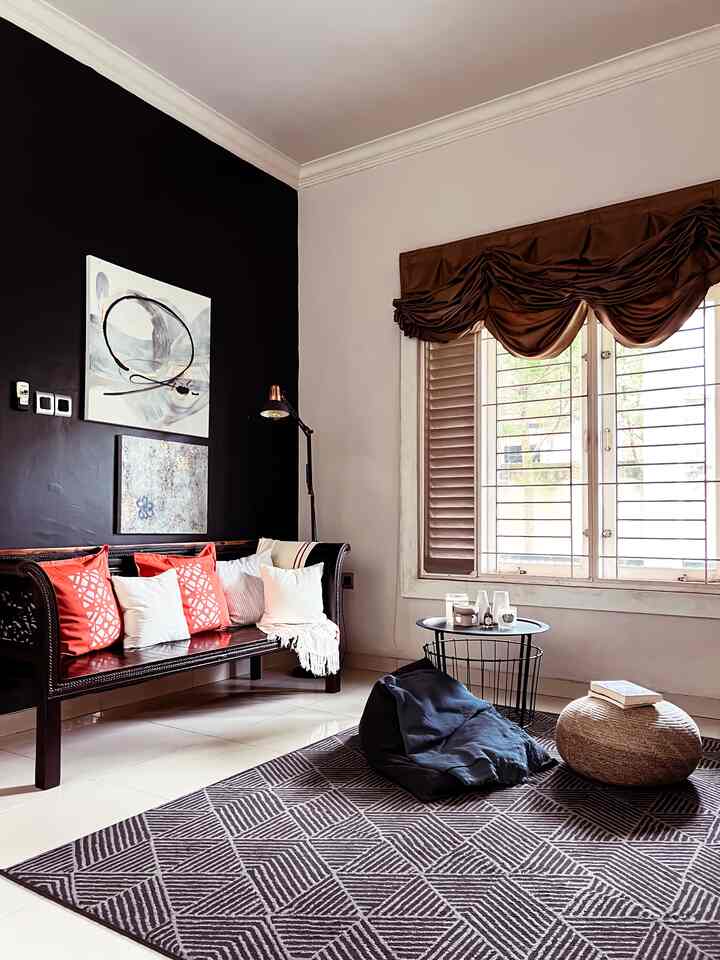 Living room with black accent wall and brown curtains, featuring vintage wooden sofa with terracotta cushions and a patterned rug creating a cozy atmosphere