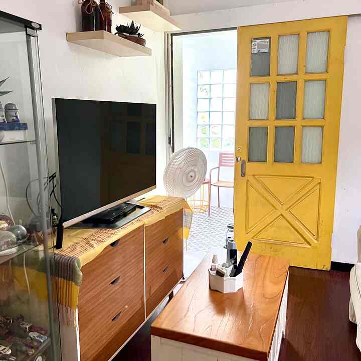 Bright white-walled small living room featuring a yellow door, wooden furniture, and a cozy coffee table