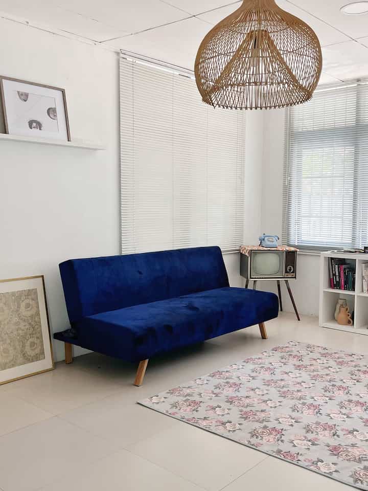 White and wood-toned vintage retro minimal living room featuring a blue sofa bed and rattan pendant lamp