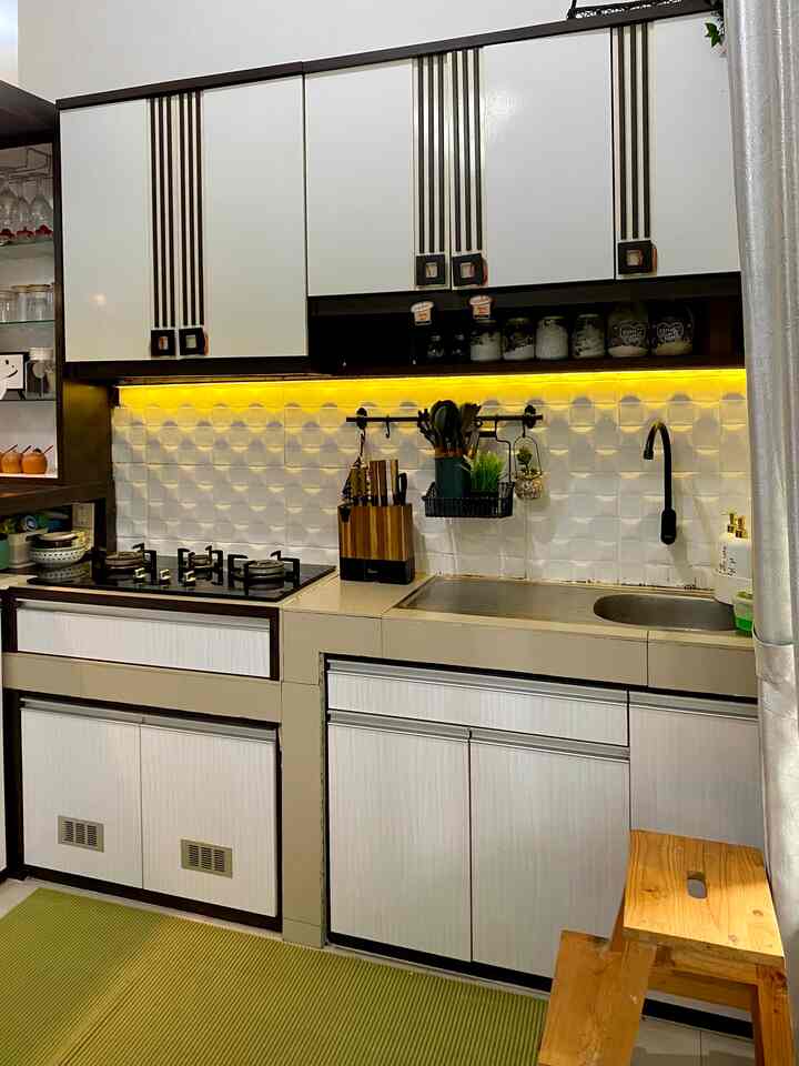 White and beige toned kitchen featuring upper and lower cabinetry, a wooden stool, and neatly organized kitchen utensils with a clean atmosphere