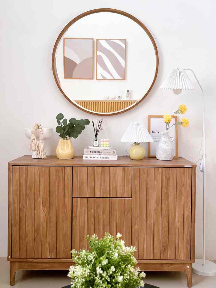 A simple and natural entrance space with white walls and a wooden closet, featuring a round mirror and floor lamp as decorative accents