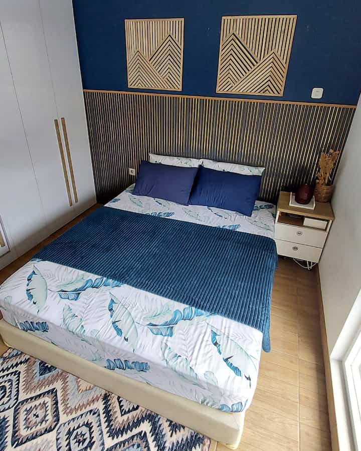 Natural tones and navy blue dominate this bedroom featuring a wooden wall panel art, bed, and nightstand, creating a simple atmosphere