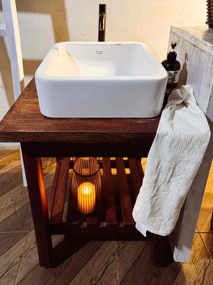 Natural-style bathroom space featuring white basin on dark wood stand with towel and candle for warm ambiance