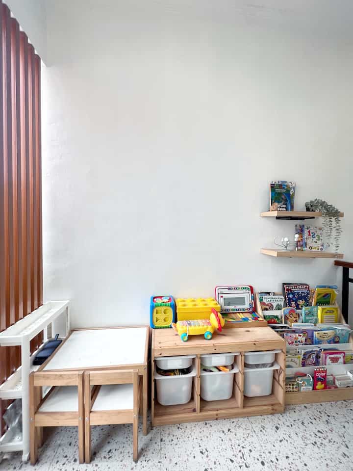 White-walled children's storage area featuring natural wood furniture, kids' desk, and organized toy storage with a clean atmosphere