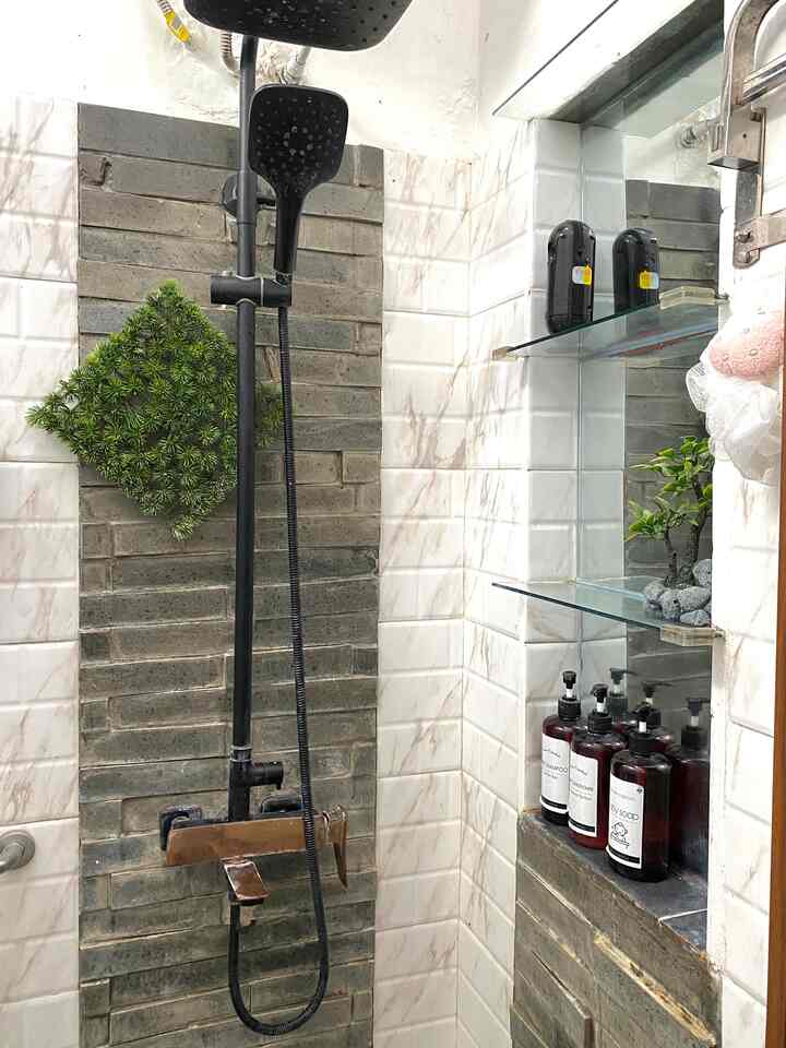 Bathroom shower area with gray brick and marble-effect tiled walls, featuring a black shower column and shampoo bottles neatly arranged