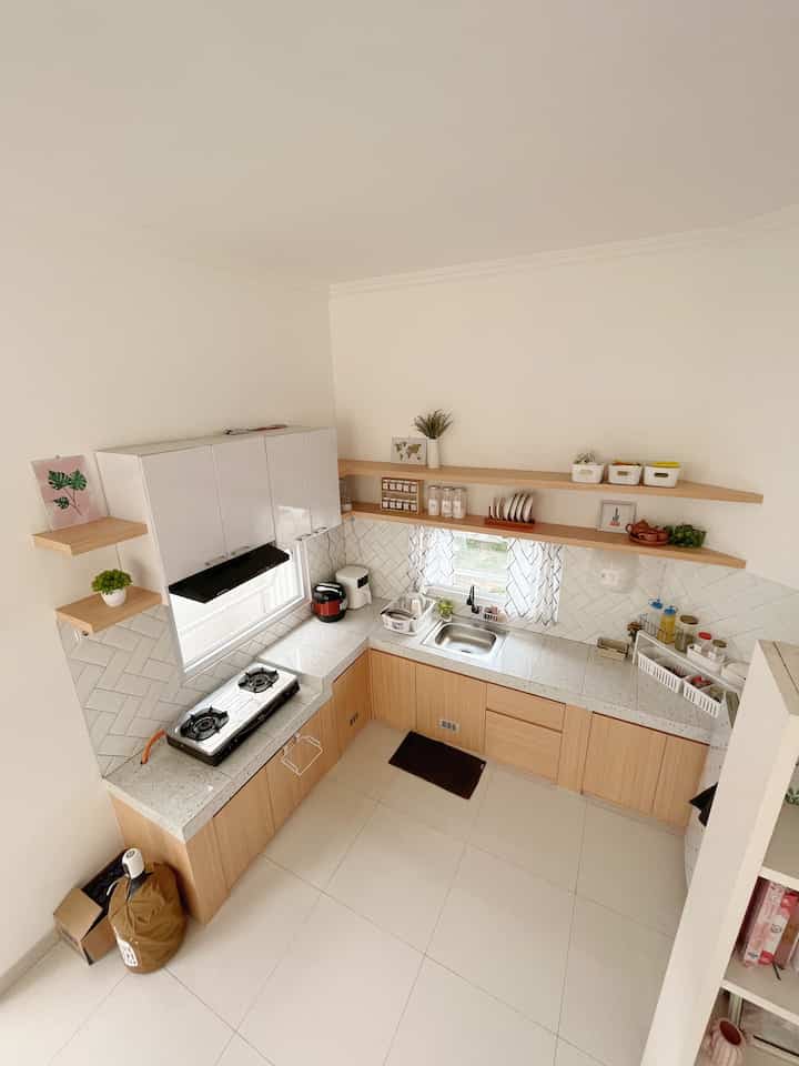L-shaped kitchen with white walls and wood-tone cabinets, featuring clean natural decor and cozy atmosphere