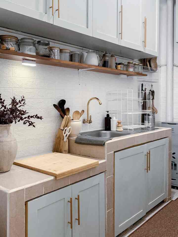 Simple natural-toned kitchen featuring white walls, brown wood cabinets, a sink with golden faucet, and open storage shelves