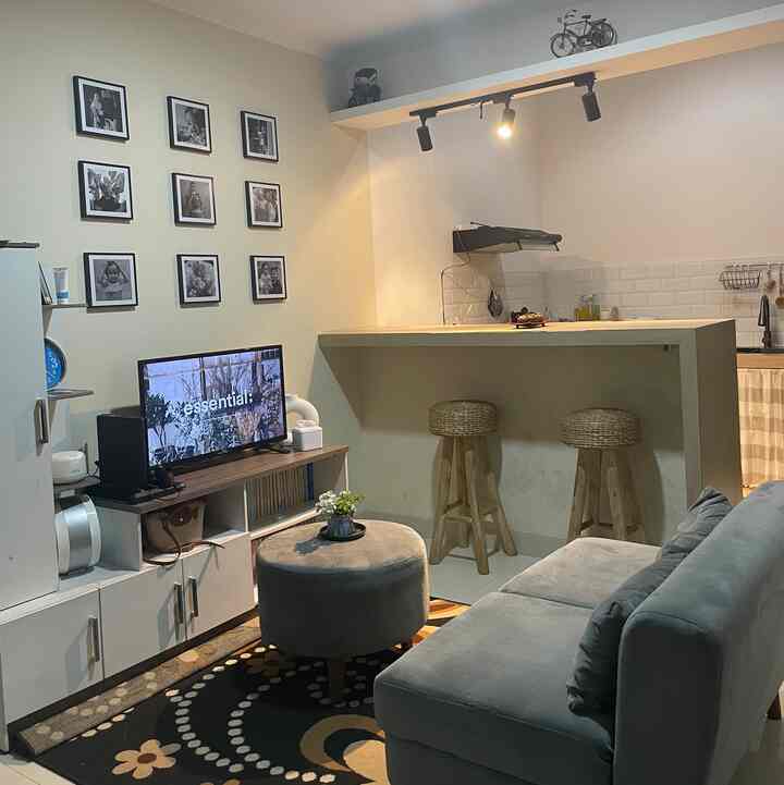 White and gray toned living room featuring sofa, TV stand, kitchen area and picture frames in a minimalist setup