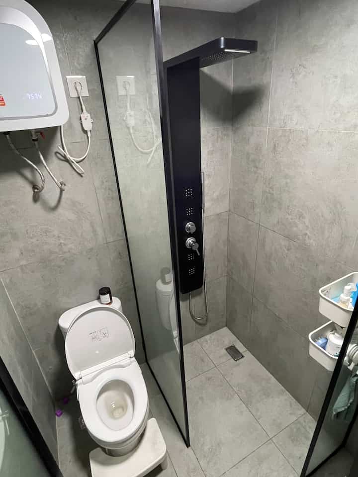 Gray tiled compact bathroom featuring white toilet, black shower panel, and a scented candle creating a clean aesthetic
