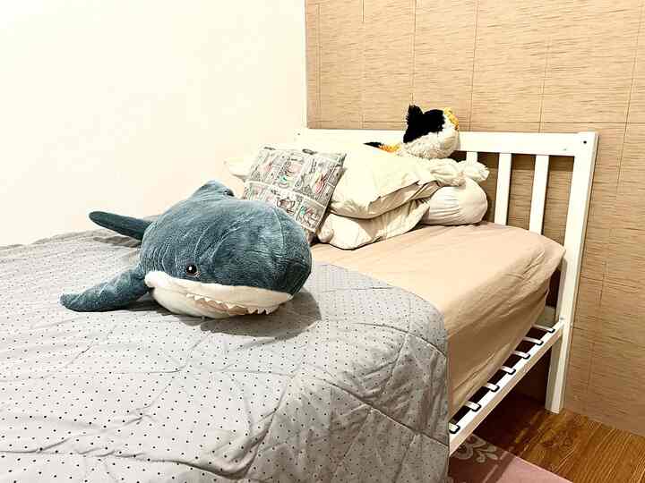 Bright-toned kids' room featuring white bed and blue stuffed shark in a simple setting