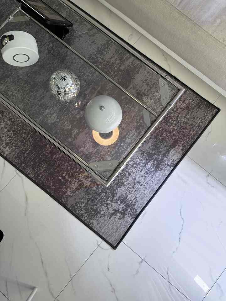 A living room space featuring a glass table with a silver and gold disco ball ornament, purple-toned carpet, and a marble floor with white veining