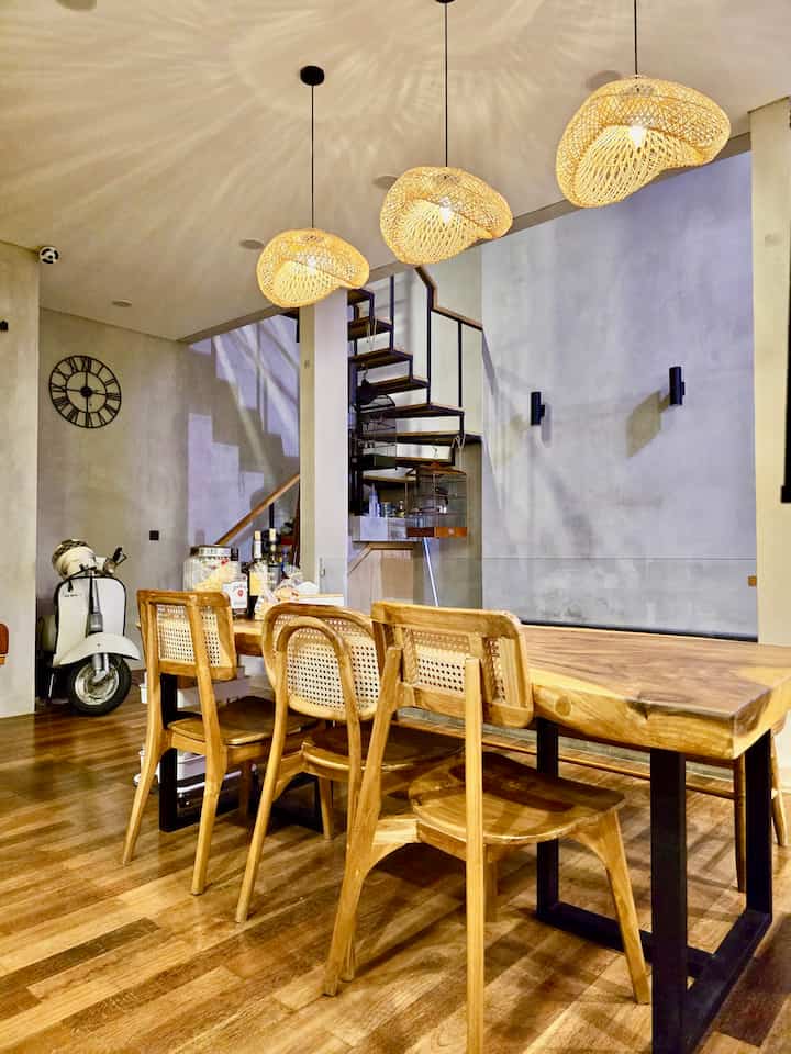 Ruang makan ini adalah tempat kami  berkumpul dan tempat kami biasa menerima tamu. Saat membangun rumah buaran, sempat terpikir untuk membuat island table di antara kitchen set dan meja makan. Namun karena keinginan memiliki meja makan cukup tinggi untuk keluarga besar, akhirnya rencana itu dikalahkan. Meja makan ini terbuat dari kayu dengan sisi-sisinya yang tidak simetris. Pemilihan kursi makan, juga sengaja tidak seragam, dengan bench di salah satu sisi. Jika tamu kami sedang banyak, kami menggunakan bench “bakso” ke kedua sisinya.
Di siang hari, meja makan ini terkadang berubah fungsi menjadi meja kerja. Sementara di malam hari, mood biasanya cukup dimanjakan dengan permainan sinar cahaya dari lampu dekoratif dan lampu sorot dari kolam renang.

#StylingRuangMakan #DiningRoomStyling #InspirasiRuangMakan #TropicalHouse #RumahTropis #IndonesianHomes #InspirasiRumah