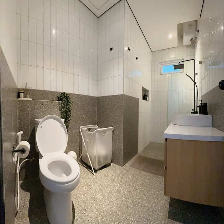 Modern bathroom with white and grey terrazo tiles, featuring black shower fixtures and wood tone cabinet in a clean layout