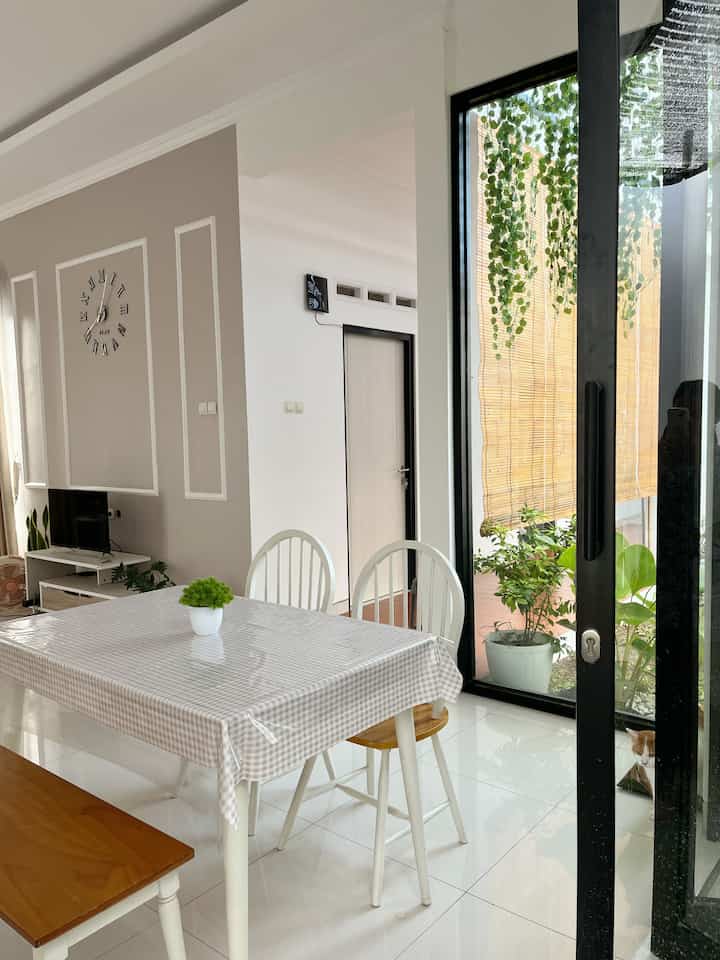 Bright dining room with white and beige tones, featuring a dining table, chairs, and indoor plants creating a cozy atmosphere