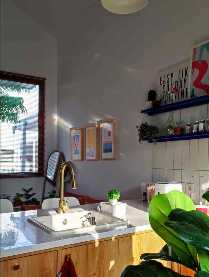 A white and wood tone kitchen featuring a gold faucet and plants, creating a natural and warm atmosphere