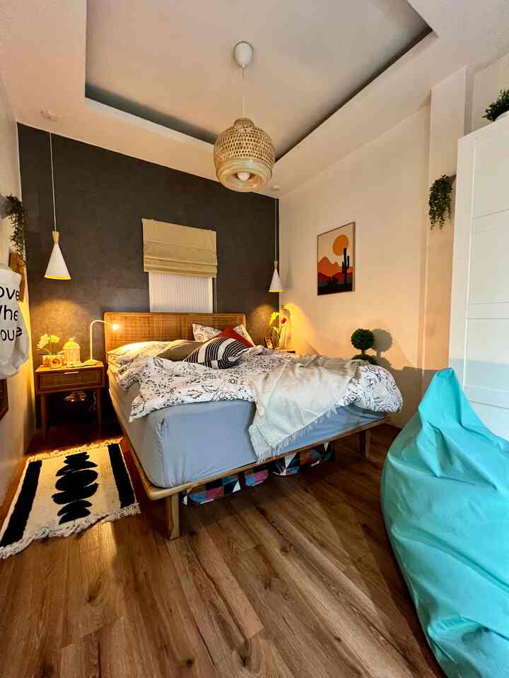 Cozy bedroom with warm wood tones and vintage style, featuring a rattan bed at center, pendant lights, a blue bean bag, and a small rug beside the bed