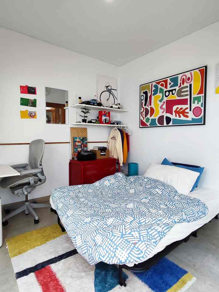 Bright white and blue toned bedroom featuring a centrally placed bed and red chest of drawers in a clean, compact space