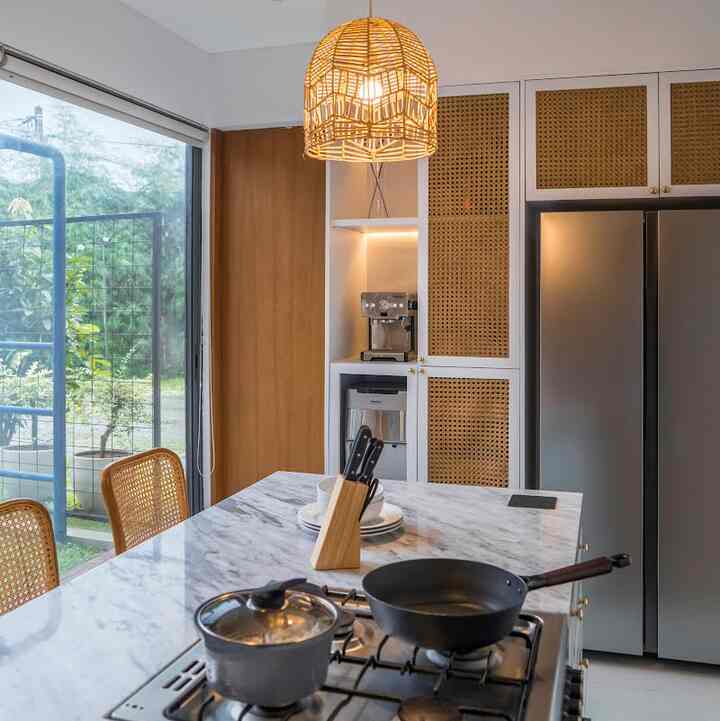 Modern kitchen blending wood tones and silver appliances, featuring a marble kitchen island and rattan pendant light