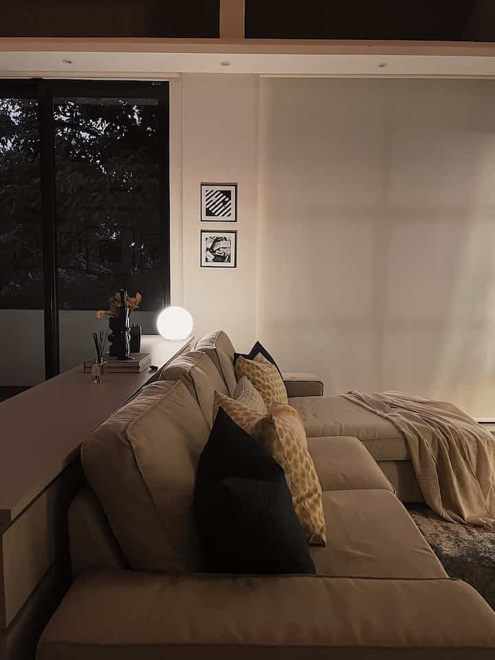 Beige-toned living room featuring large light brown sofa with cushions, round lamp, and cozy blanket creating a natural atmosphere