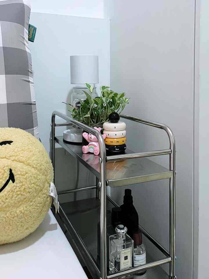 White and stainless steel toned small room featuring a multi-tier trolley rack with a lamp, plant, and decor next to the bed, creating a neat atmosphere