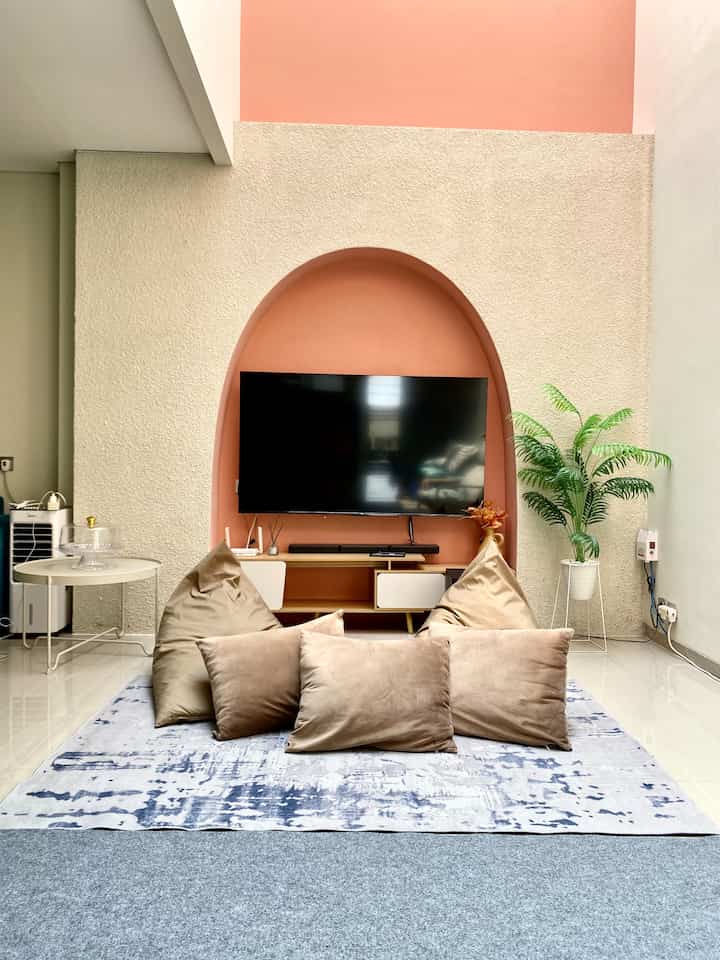 White and beige tone living room featuring soft brown cushions and bean bags in front of a mounted TV set within an arch-shaped alcove, creating a cozy atmosphere