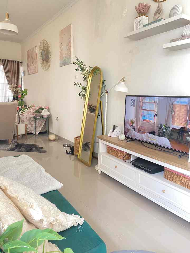 Bright white and gold toned living room featuring green sofa, standing mirror, and TV stand with natural atmosphere