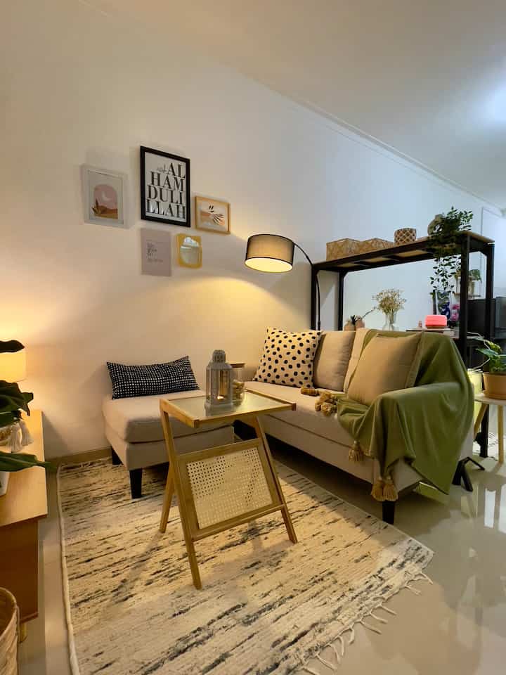 A cozy small living room in warm natural tones featuring a beige sofa, wooden side table, and wall art