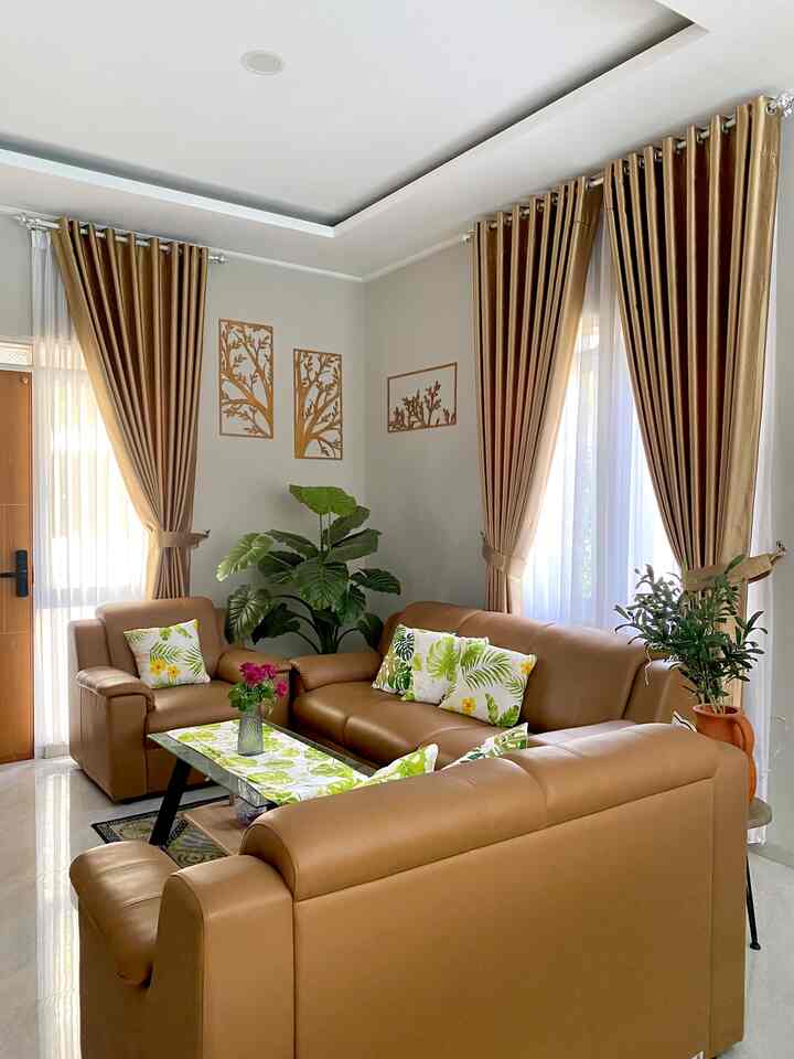 Warm brown and natural green toned living room featuring brown leather sofa, plants, and curtains creating a cozy atmosphere