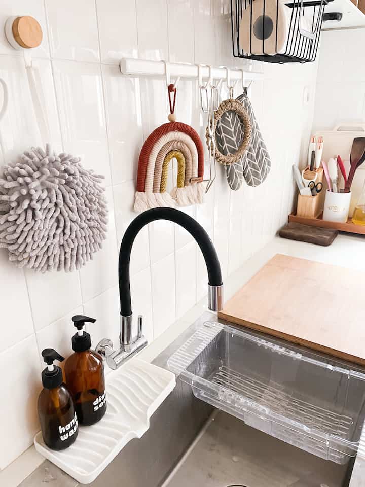 White and silver kitchen space featuring a transparent drain rack, single-handle faucet, and neatly arranged towel hooks and kitchen utensils