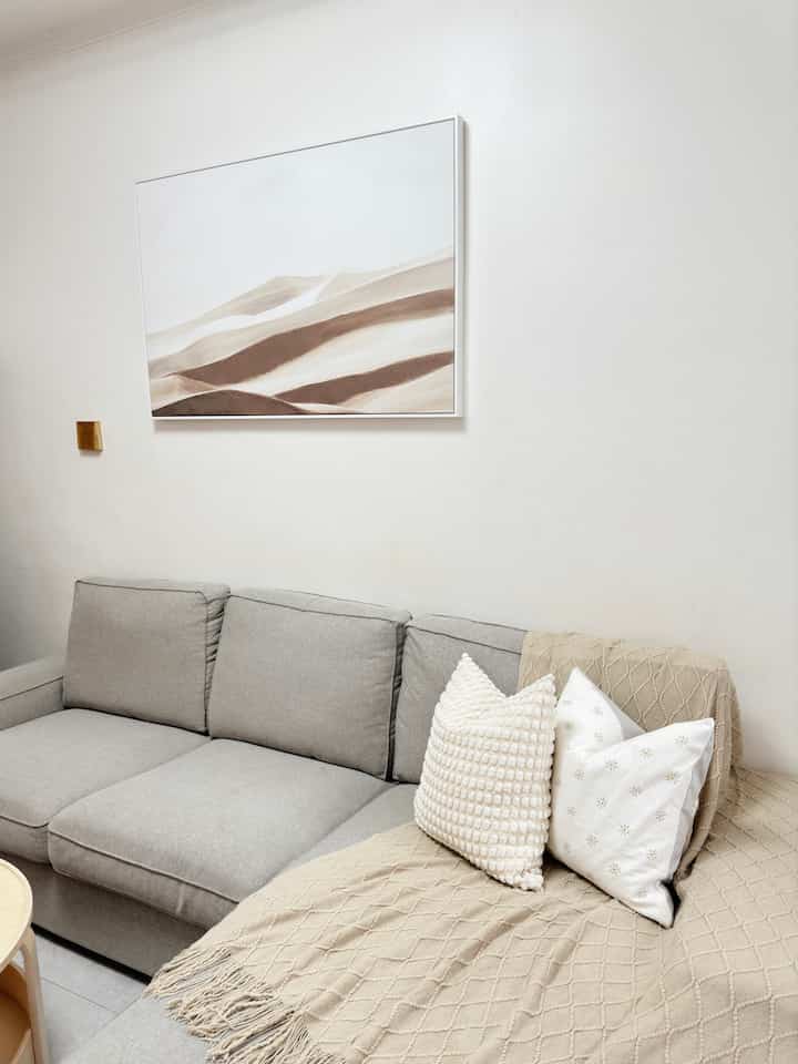 Natural and simple living room in gray and beige tones featuring a sofa with cushions and desert dunes artwork on the wall