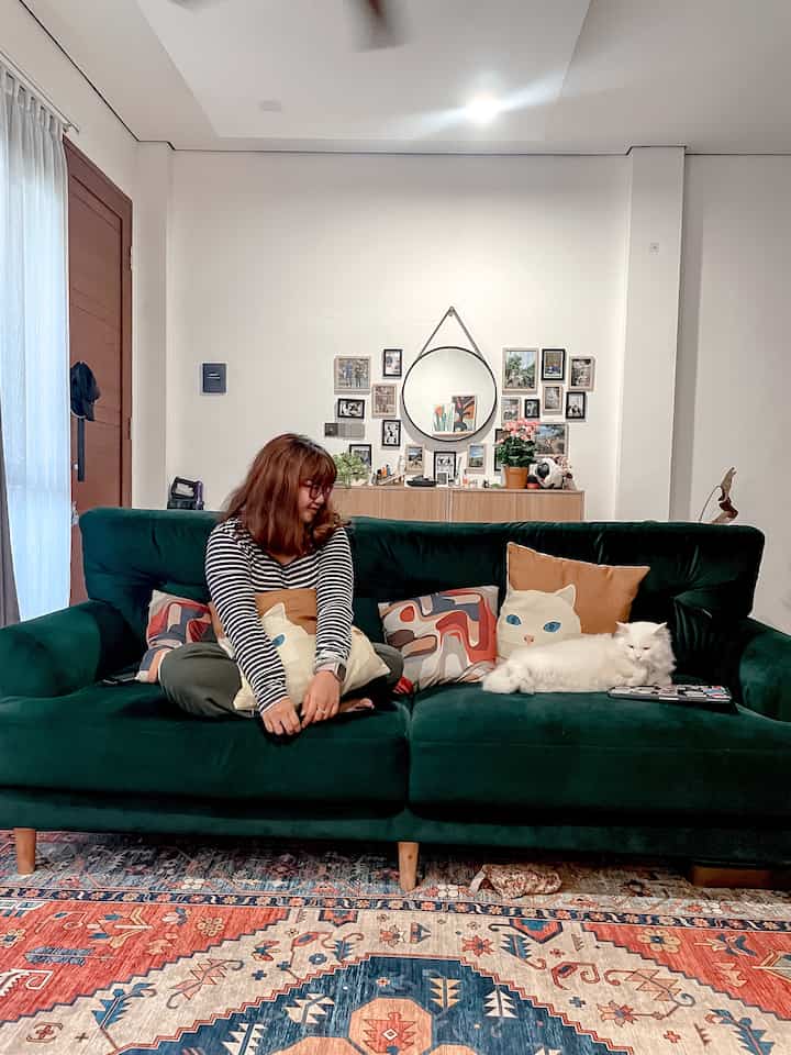 Living room featuring a dark green sofa and patterned carpet, with a cat, picture frames, and natural modern decor