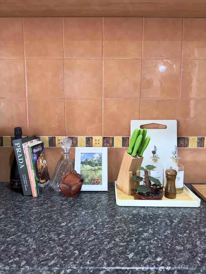 Kitchen space with warm brown tiled wall and gray marble countertop featuring a wooden tray and knife set neatly arranged