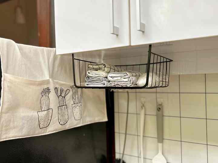 A neat kitchen space featuring a black and white color scheme, with folded towels organized in a metal rack beneath the cabinet, showcasing smart storage ideas