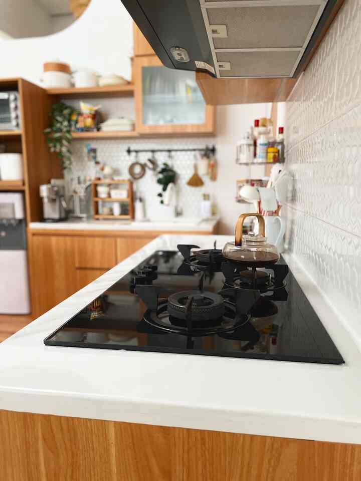 A compact kitchen with wood tone cabinets and white tiled backsplash, featuring organized storage and a sleek cooktop for a cozy cooking space