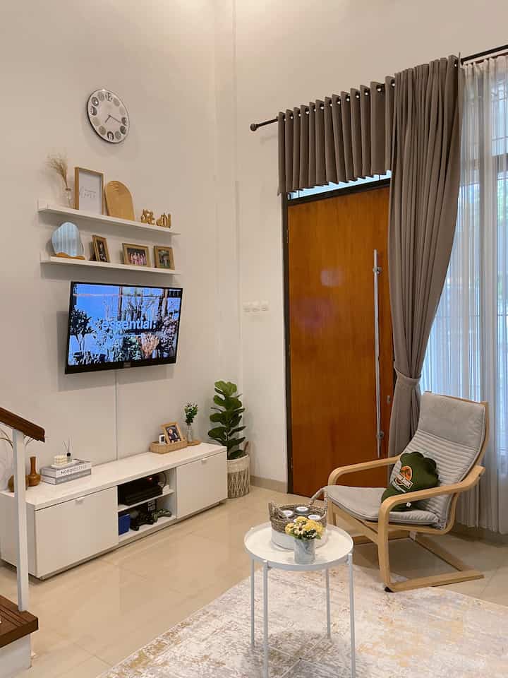 Beige and gray toned living room featuring wooden armchair, small round coffee table, TV, and plant in a simple modern space