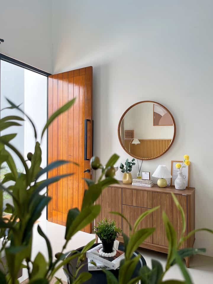 Natural tone entrance space featuring wooden furniture, a round mirror, and decorative plants creating a warm atmosphere