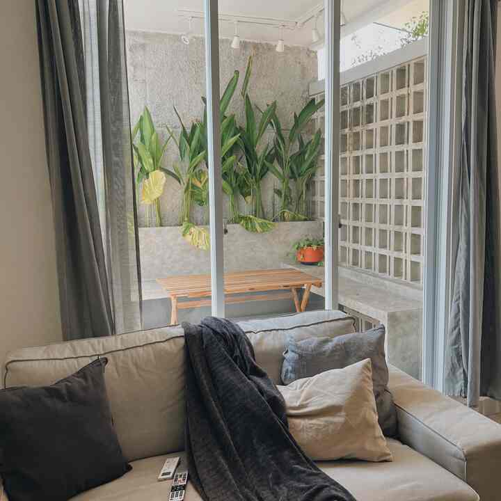 Beige and black toned living room with a large sofa, curtains framing sliding glass doors revealing a sunlit terrace with plants
