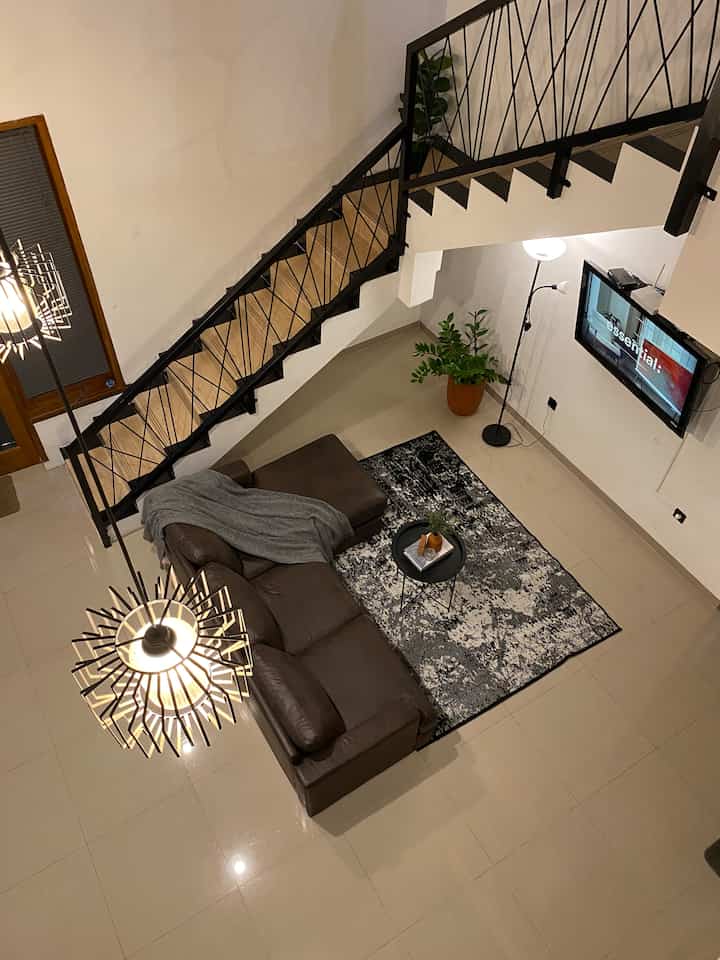 Modern living room with brown sofa and black stairs, featuring a stylish floor lamp and carpet creating a cozy atmosphere