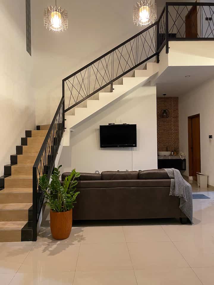 Natural color and brown toned living room featuring stairs, sofa, and wall-mounted TV with cozy atmosphere