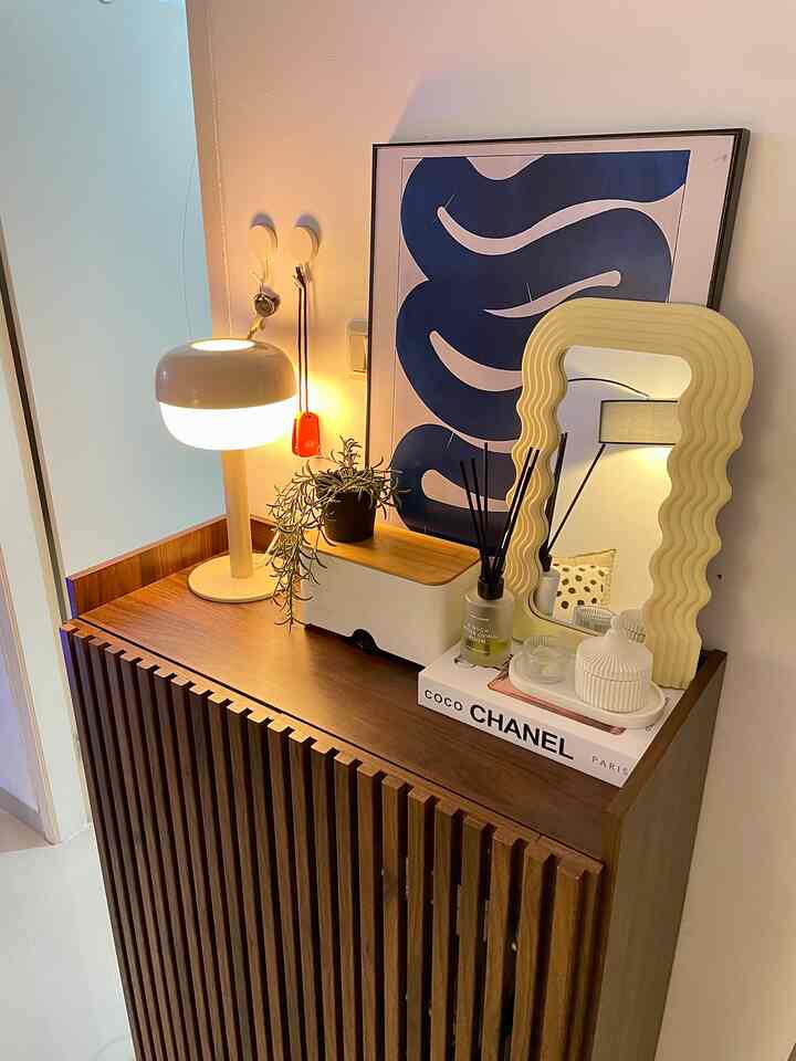 Wood tone vanity and wavy mirror in an entrance area with white background walls and floor