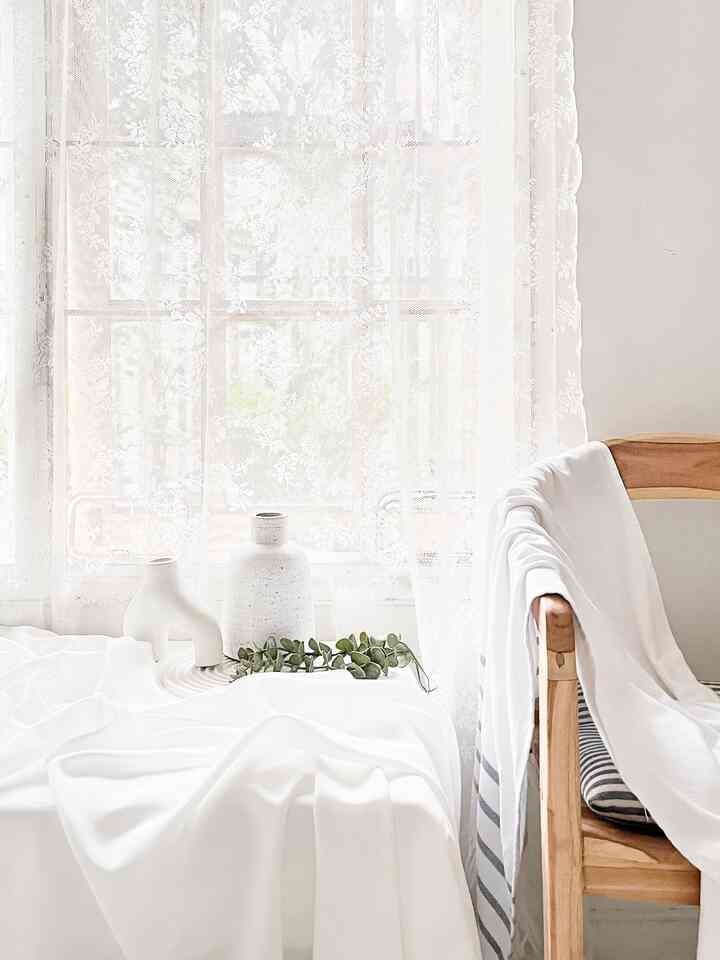 Bright and natural living room featuring white and natural wood tones, lace curtains, and Scandinavian-style vases