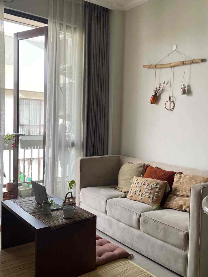 Beige-toned living room featuring a beige sofa, coffee table, blackout curtains by the window, and natural decor creating a cozy atmosphere