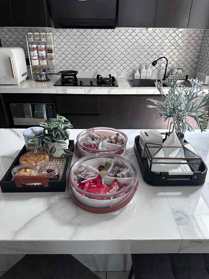Modern kitchen with white marble countertop and black cabinets, featuring organized trays and snacks on the clean surface