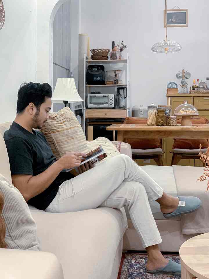 White and beige toned living room featuring a natural interior with a man reading on a beige sofa